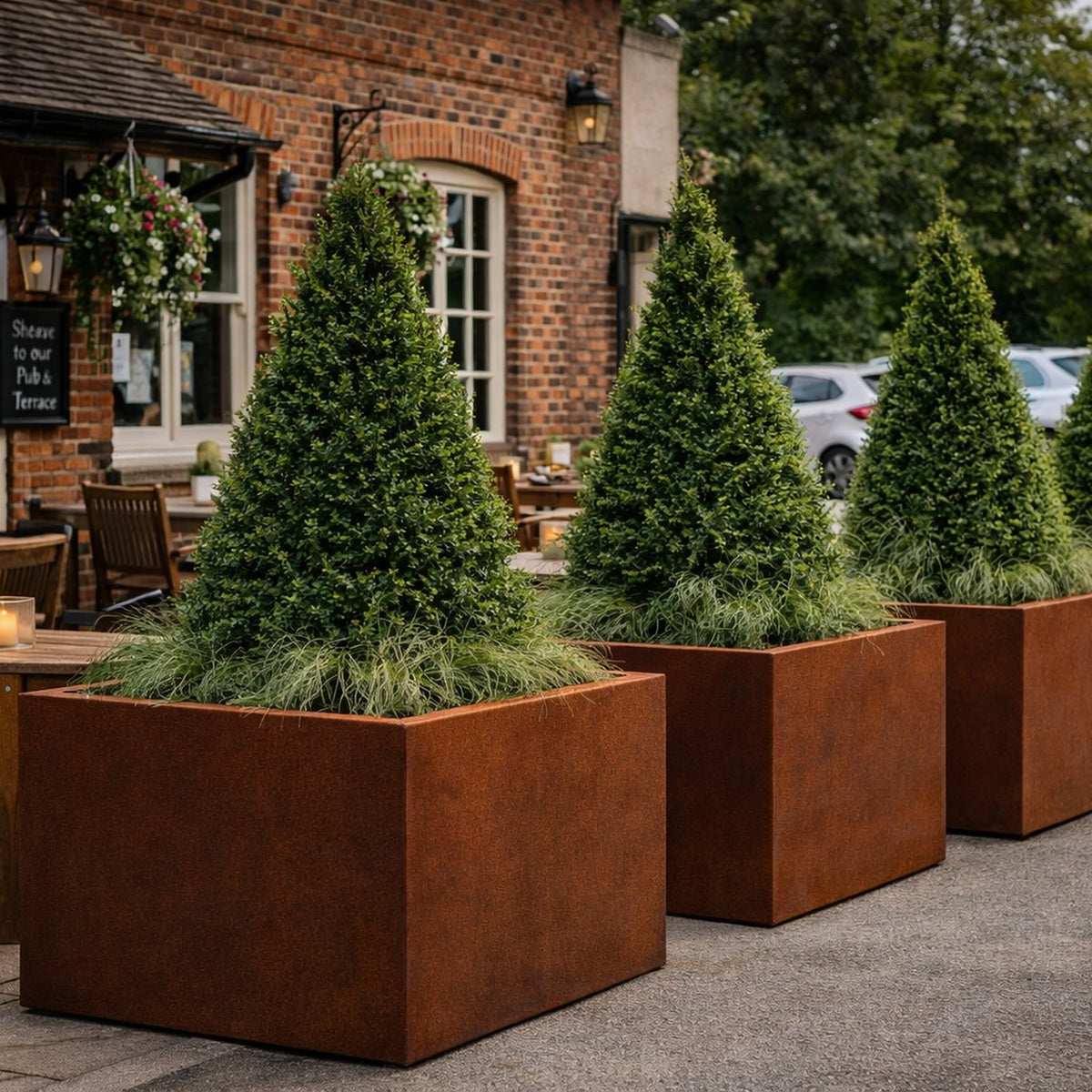Corten steel cube planters with pyramid bay trees screening a pub terrace and car park, durable commercial outdoor planters UK
