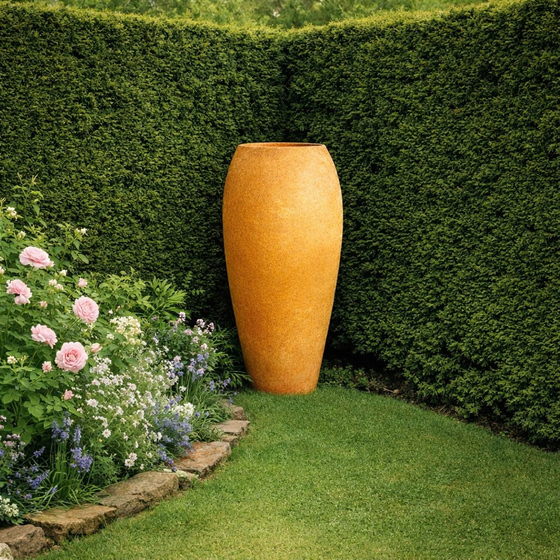 Large terracotta outdoor vase planter styled in English garden corner with yew hedge and blooming flowers